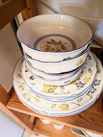 Stack of Villeroy & Boch fine china bowls and plates with yellow and blue floral pattern on shelf.