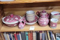 Porcelain set displayed on wooden shelf including covered dish, teapot, cruet, bowls stacked inside serving plate.