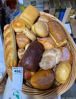 Wicker basket filled with highly realistic fake bread including baguettes, loaf breads, rolls, and bagel shapes, shown from overhead angle.