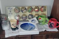 Full lot showing 12 glass nutcracker Christmas ornaments in box with gold tops, 2 Star Wars mugs, Royal Copenhagen plate in box, beige boot-shaped cup, and glass shaker with white granular contents