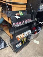 Photo showing whole black metal display rack with various items arranged on shelves including football and card packs.