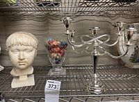Shelf display showing plaster head statue, glass vase with hand painted wooden eggs, and silver candelabra.