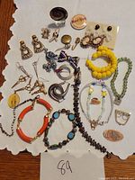 Top-down image of various costume jewelry items including earrings, pins, and bracelets arranged on a white cloth with the number 89 written below