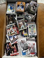 Top view of large box filled with various sports trading cards including baseball, basketball, football, and hockey cards.