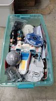 Top-down view of plastic bin containing various Star Wars toys including Millennium Falcon, TIE Fighter, character banks, and AT-AT head toy.