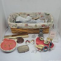 Woven basket with floral fabric liner, vintage pins, sewing kit tin, Sheaffer pen, perfume bottles, trinket dish, and metal bell displayed on table.