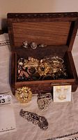 Wood box open showing a collection of jewelry inside and an assortment of jewelry pieces arranged in front including 3 dress clips and a gold-tone lion head scarf clip.
