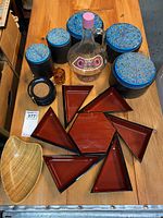 Five black ceramic canisters with blue decorated lids, red lacquer dishes, coasters, tea light holder, bowl and decanter arranged on wooden table