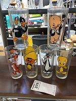 Photo showing the full set of six vintage Looney Tunes drinking glasses with characters Daffy Duck, Porky Pig, Taz, Speedy Gonzales, Sylvester, and Tweety Bird.