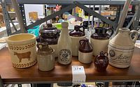 Full view of 9 stoneware items including 8 crock jugs and 1 bottle chiller on wooden table.