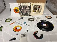 Photo showing approximately 21 Beatles 45 RPM vinyl records with various sleeves and labels visible including Capitol and Apple Records.