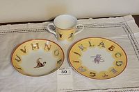 Front view of the porcelain set including cup, plate, and bowl with animal alphabet designs arranged on a white cloth.