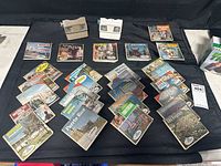 Two View-Master 3D viewers and 20+ photo reel packets arranged on black cloth, reels featuring diverse travel and entertainment subjects.