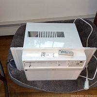 LG white portable air conditioner with front and top vents along with white remote on top of the unit.