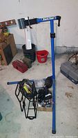 Wide view of the Park Tool PCS-9 bike repair stand with accompanying bike parts and tool boxes on the floor in a garage setting.