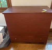 Front view of the red painted wooden blanket chest with two wooden knobs on the bottom drawer.