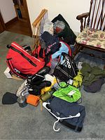 Overview of camping gear including backpacks, shoes, water bottles, sweatshirt, and walking sticks scattered on carpet.