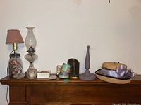 Wide view of wood surface holding two glass lamps, straw hat, decorative cup, box jewelry, and glass bookends.