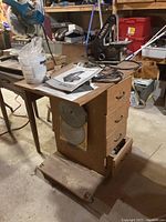 Workbench with attached drawers, mounted circular saw blade, and several items on top including cords and paper manuals.