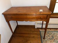 Front view of the wood desk, showing its single drawer and turned legs.