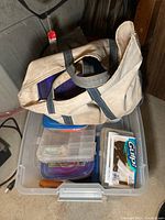 Wide angle image showing beige canvas fishing bag on top of multiple plastic tackle boxes containing fishing accessories.
