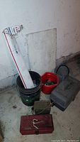 Wide shot of buckets, tackle boxes, and a boxed fishing lure, showing the general lot contents and condition
