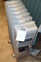 Side view of the white oil-filled heater with a tag number 339 on top, showing control panel and ventilation slots.