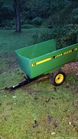 Full side view of John Deere green utility cart with yellow branding and black tongue hitch on grass surface.