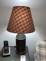 Table lamp with brown plaid fabric shade on a side table, closed door on the lamp base is visible.