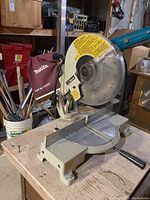 Close-up of Makita LS1030 mitre saw showing blade, blade guard with warning label, dust collection bag, and handle.