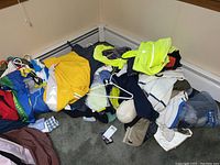 Pile of assorted cycling apparel including jackets and shirts with some sweatshirts in a corner of the room.
