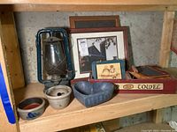 Photo showing vintage blue metal lantern, framed print, wooden wall plaque, mini pottery bowls and heart-shaped bowl on a wooden shelf