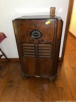 Front view of large wooden cabinet radio with tuning dial and control knobs showing worn wood and scratches