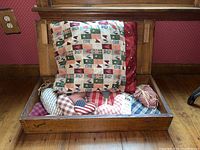 Wooden box opened showing assorted fabric craft pillows inside including heart-shaped and patchwork pattern pillows