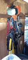 Gas-powered weed wacker hanging on wall with orange, black, and white components.