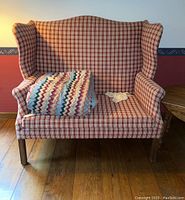 Front view of the wingback settee with plaid upholstery and linens on the seat.