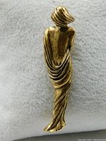 Backside view of the brass brooch showing the detailed draping and back of the woman figure.