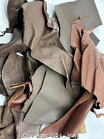 Top-down photo showing assorted irregularly shaped leather pieces in various shades of brown with different textures including smooth, pebbled and glossy finishes, displayed overlapping on a white background.