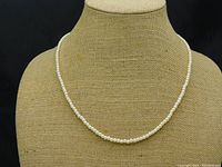 Front view of the cream pearl necklace displayed on a beige fabric stand, showing the uniform strand of pearls against black background.