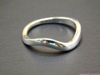 Side angle of polished silver-colored modern wave ring on black background showing its smooth, rounded design.