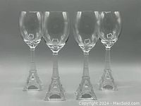 Four clear wine glasses with stems shaped as Eiffel Towers, shown in full view against neutral background.