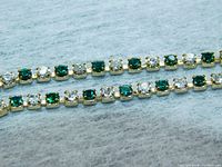 Close-up of the bracelet showing alternating round emerald green and clear cubic zirconia stones set in gold-colored metal.