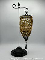 Black metal tabletop candle holder with amber bead hanging cage on a curved hook with a round stepping base.