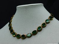 Front view of the Italian Florentine necklace displayed on a mannequin bust showing the hunter green translucent oval glass beads with gold edging and gold round beads separating them.