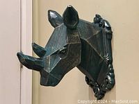 Side angle showing geometric facets, dark green with silver highlights, double horns, ears, and ornamental base for wall mounting.