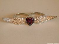 Front view of Swarovski Elements Jacqueline Kent double finger ring featuring mauve heart-shaped Swarovski crystal and clear crystal wings on a silver metal base.