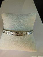 Front view of the silver bangle bracelet on a white cushion showing the Mayan embossed design and overall condition