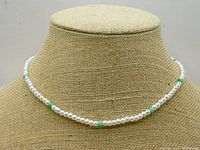 Full view of pearl necklace displayed on a textured stand showing white/cream pearls and interspersed jade green beads.