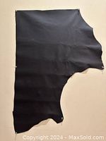 Full view of the irregular shaped black leather piece pinned to a wall, showing size and shape.
