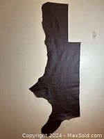 Photo showing the full irregular shape of the dark brown leather piece against a beige background